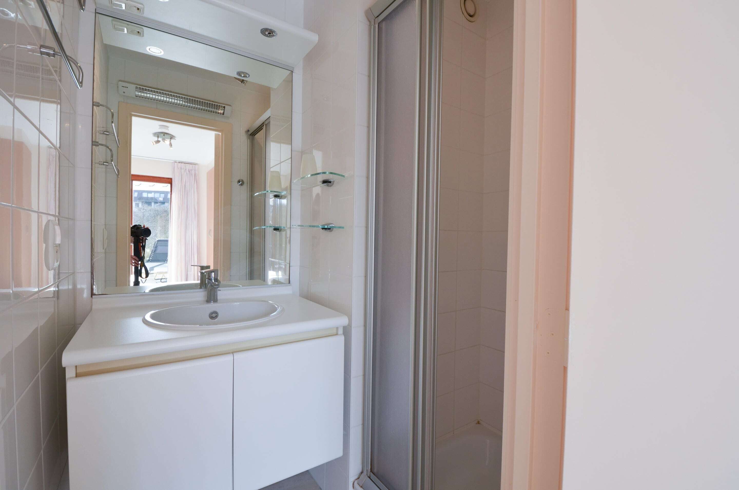 A bathroom with a white sink, a glass shower enclosure, and a large mirror.