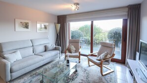Una sala de estar moderna con un sofá, sillones, una mesa de centro de vidrio y un televisor.