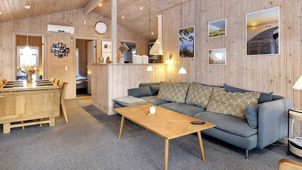 Una habitación acogedora con techo y paredes de madera, un sofá, una mesita de centro de madera y un comedor con mesa y sillas de madera.