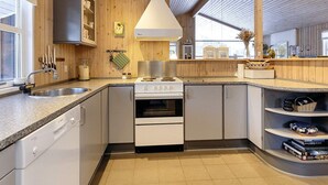 Una cocina moderna con paredes de madera, horno empotrado y pileta de acero inoxidable.