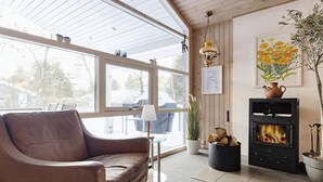 Un cuarto acogedor con un sofá de cuero marrón, una mesita de vidrio, una lámpara, una chimenea y un ventanal con vistas al exterior.
