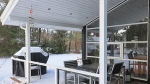 Terraza exterior cubierta con una parrilla y sillas, rodeada de nieve.