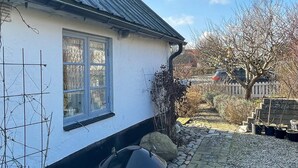 Una casa bianca con una finestra, una griglia nera e un vialetto in pietra che conduce a un cancello.