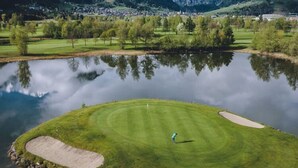 Een golfbaan met een vijver, bomen en bergen op de achtergrond.