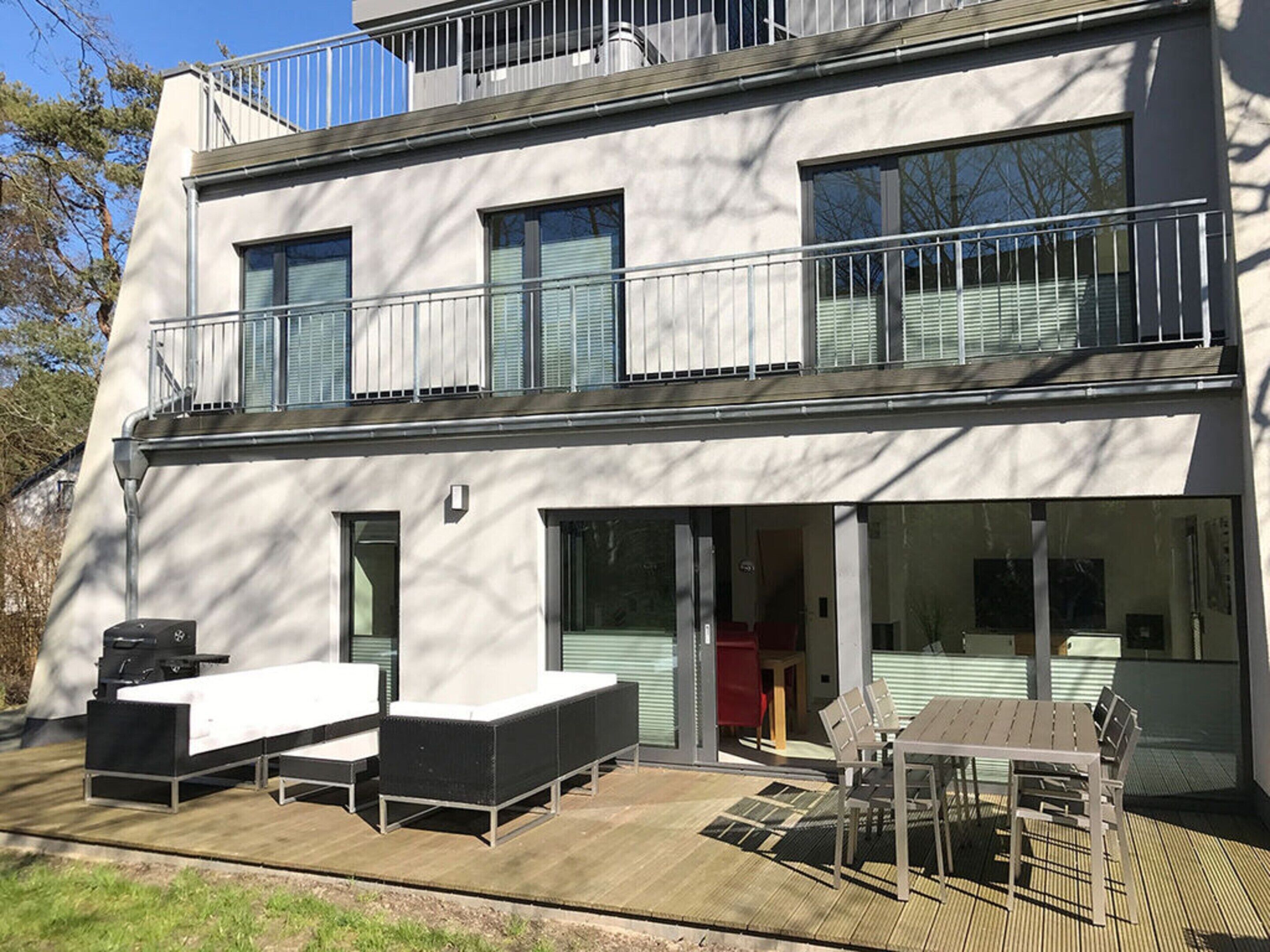 A modern two-story building with a balcony, outdoor seating area, and a sliding glass door entrance.