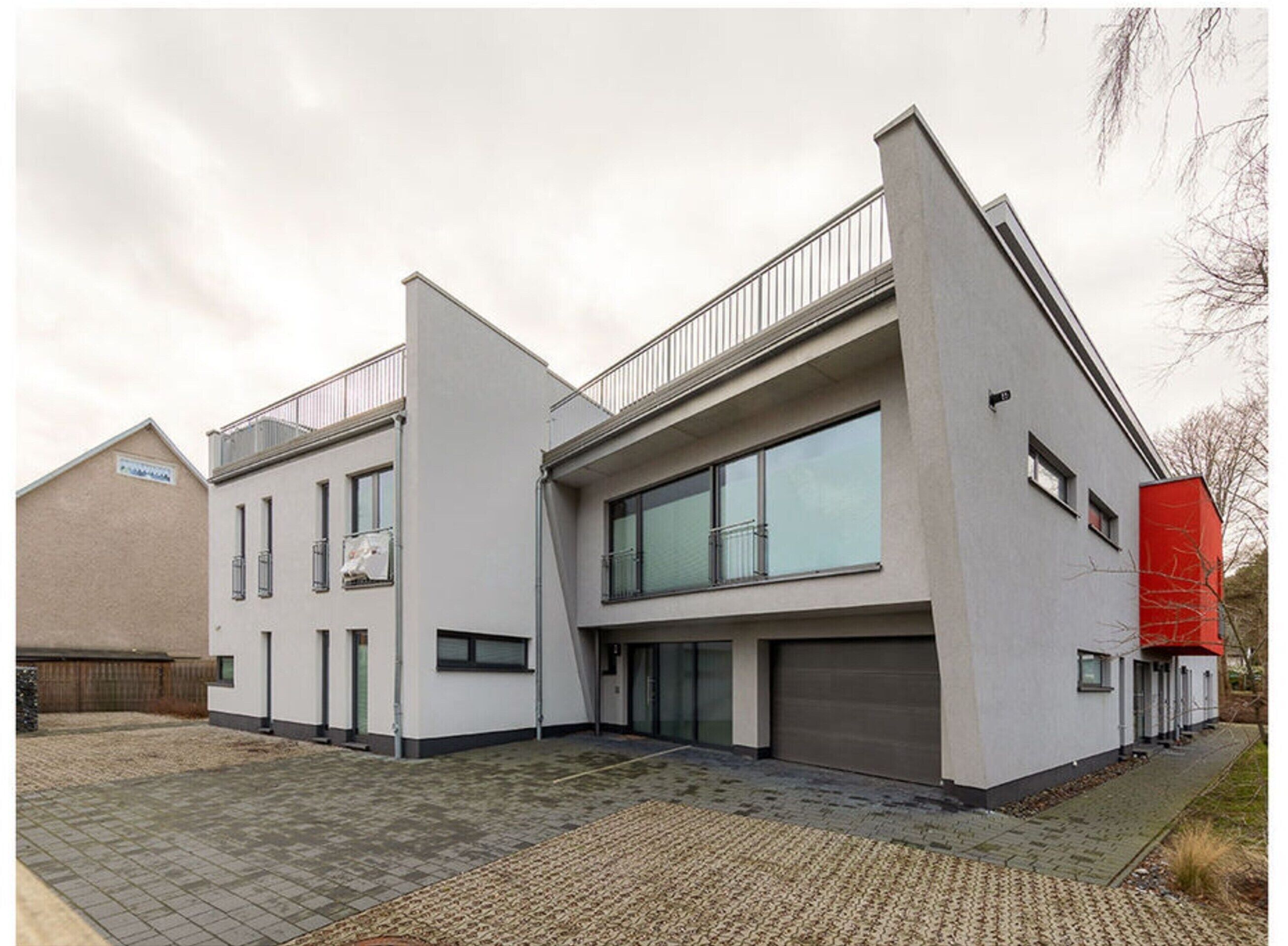 Un bâtiment moderne doté d’un toit plat, de grandes fenêtres et d’un mur d’accent de couleur rouge.