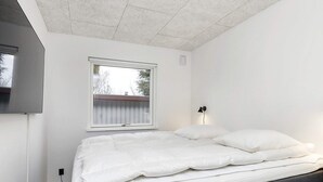 A bedroom with a bed, a window, a wall-mounted lamp, and a TV on the wall. - 4 Star Holiday Home in Vaeggerlose (Vaeggerlose)