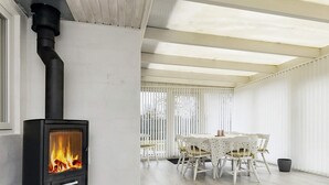 A modern room with a wood-burning stove, white furniture, and a large window. - 4 Star Holiday Home in Vaeggerlose (Vaeggerlose)