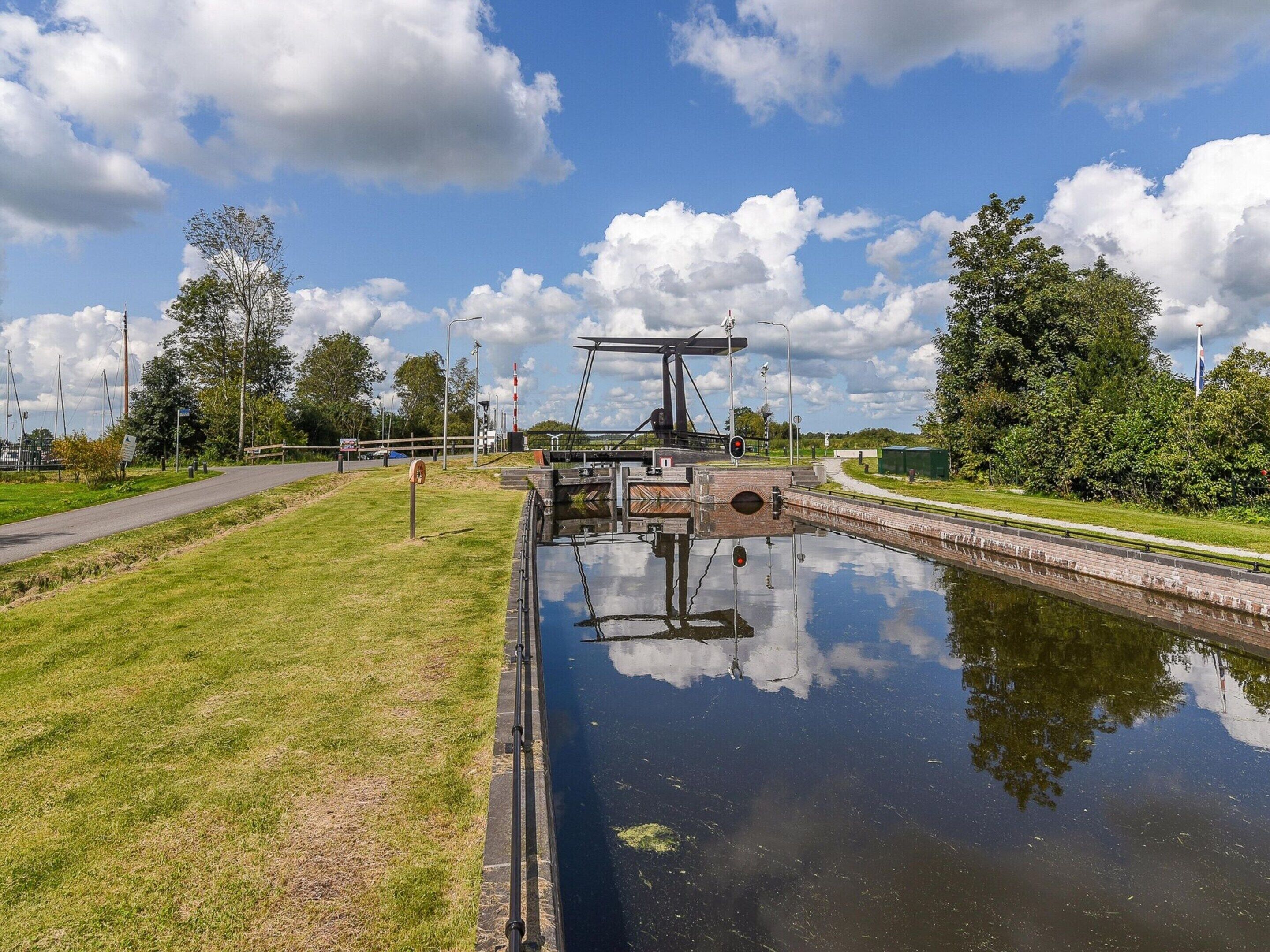 A canal lock with a bridge, surrounded by grassy areas and trees.