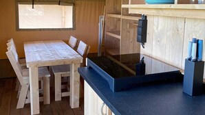 A compact kitchen with a wooden table and chairs, a black countertop, and a window with a view. - Waterfront Glamping Escape (De Veenhoop)