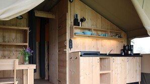 A wooden cabin interior with a kitchen area, a dining table, and a vase with flowers. - Waterfront Glamping Escape (De Veenhoop)