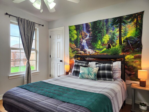 A bedroom with a bed, a window with curtains, a door, a tapestry, and two bedside lamps.