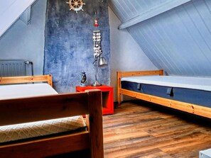 Ein kleines, gemütliches Schlafzimmer im Dachgeschoss mit zwei Holzbetten, einem roten Nachttisch, einer Wandlampe und einer Schiffslaugendesign-Dekoration.
