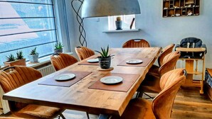 A dining area with a wooden table, orange chairs, potted plants, and a large pendant light. - Quaint Holiday Home in Lamswaarde With Garden (Lamswaarde)