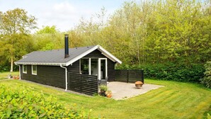 Une petite cabane moderne, dotée d’un toit en pente, d’une cheminée et d’un espace patio avec un foyer.