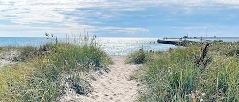 En sti af sand der fører hen til vand, med en klar himmel over sig.