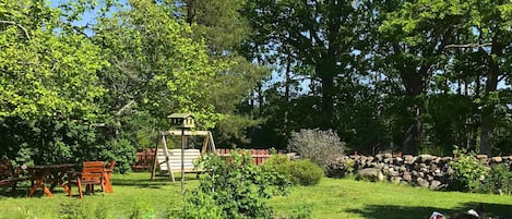 A garden with a wooden swing set, a stone wall, and a dog.