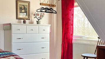 A bedroom with a white dresser, a bed with a colorful quilt, a red curtain, and a window with a view.