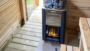 Ein Harvia Holzofen mit Feuer im Inneren, auf einem Holzboden in einem Raum mit Holzwänden und einer Bank.