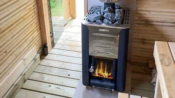 A Harvia wood stove with a fire burning inside, placed on a wooden floor in a room with wooden walls and a bench.