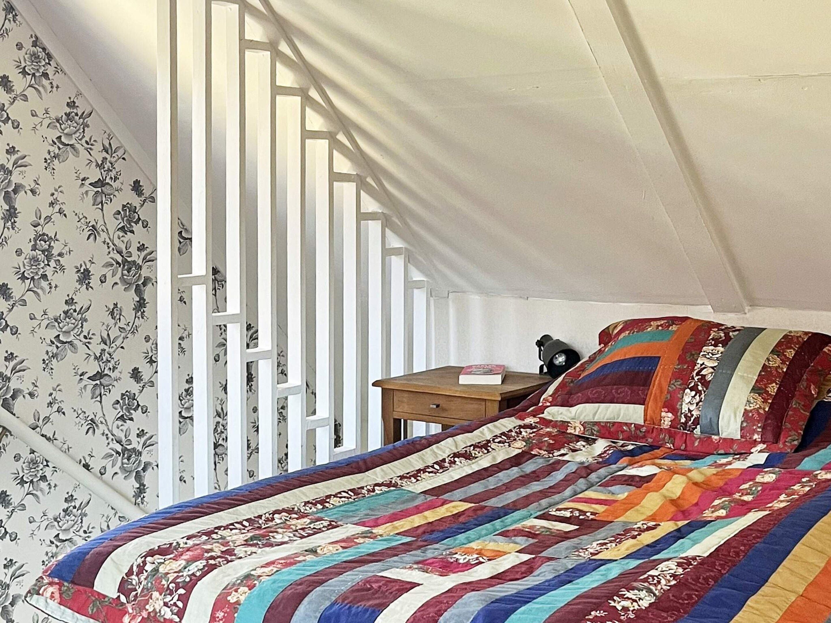 A bedroom with a bed, a nightstand, and a window with white blinds.