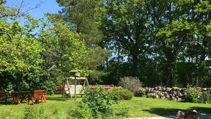 Ein Garten mit einem hölzernen Spielhäuschen, Picknicktischen und einer Steinmauer.