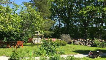 A garden with a wooden playhouse, picnic tables, and a stone wall.