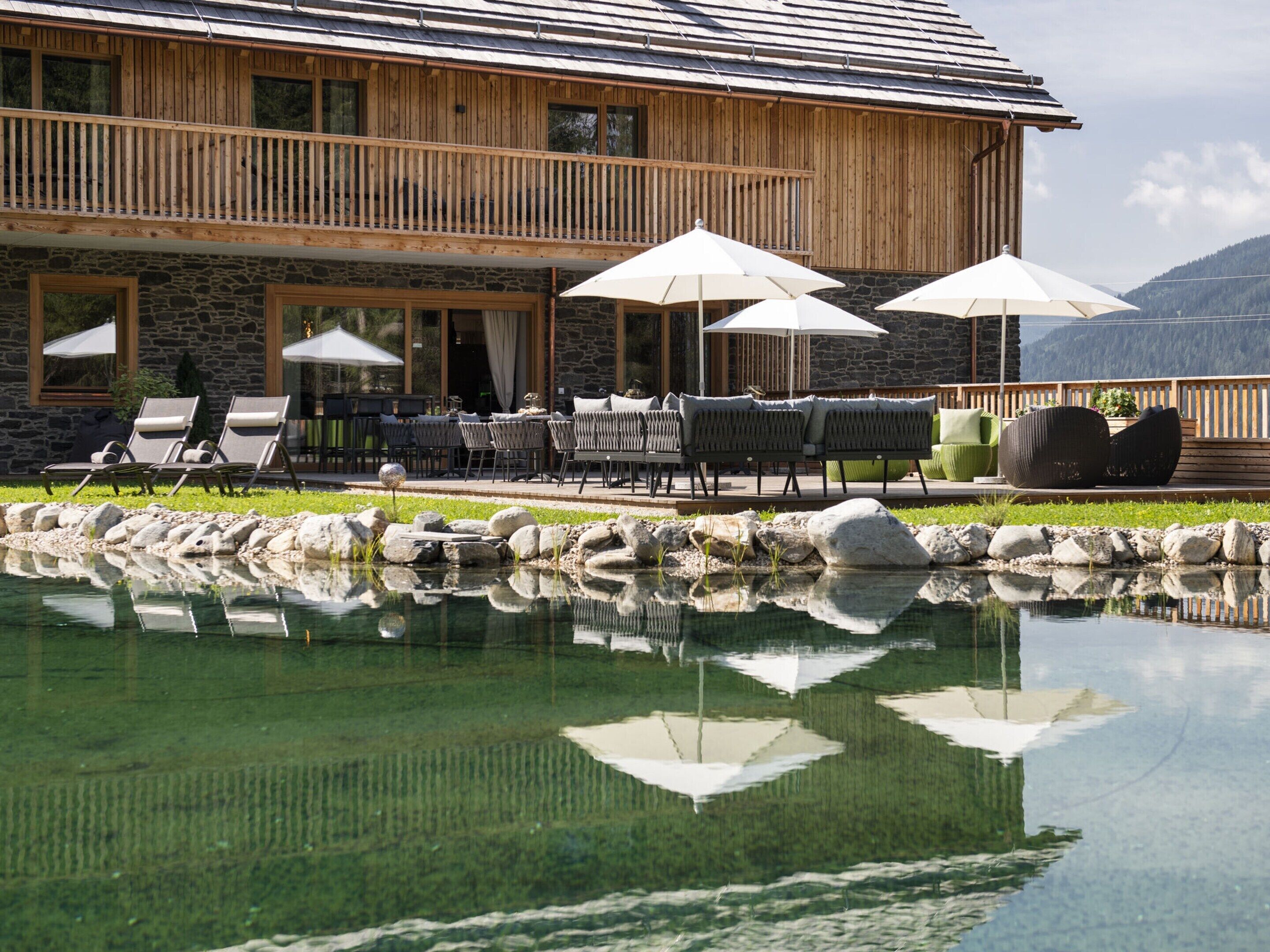 A wooden building with a stone facade, outdoor seating, and a reflecting pool.