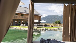 Une pièce dotée d’une grande baie vitrée donnant sur une piscine, une terrasse en bois et une vue sur les montagnes.