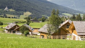 Un village rural avec des maisons traditionnelles en bois, une église et une chaîne de montagnes en arrière-plan.