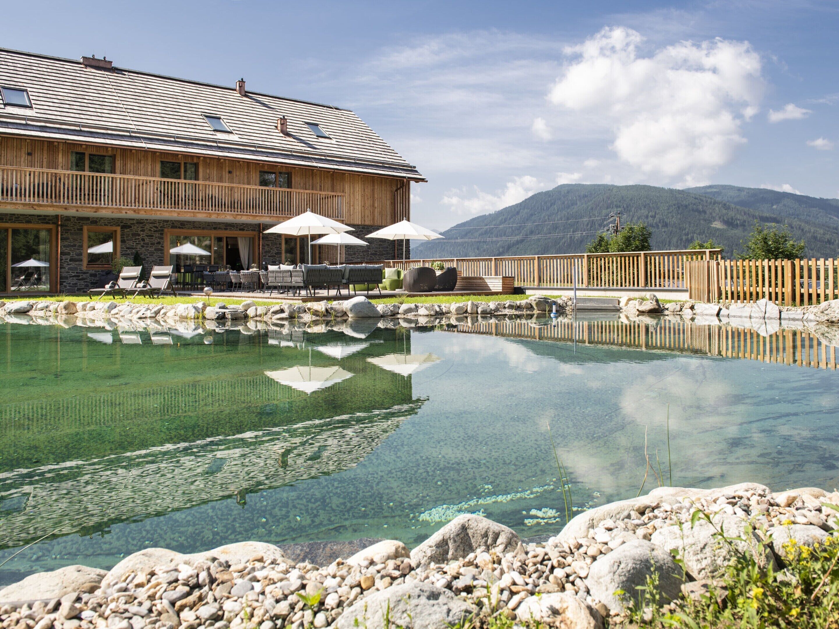 A wooden building with a pool, outdoor seating, and mountains in the background.