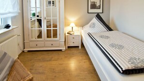 Un dormitorio con cama, un armario blanco, una mesita de noche, una lámpara y un cuadro en la pared.