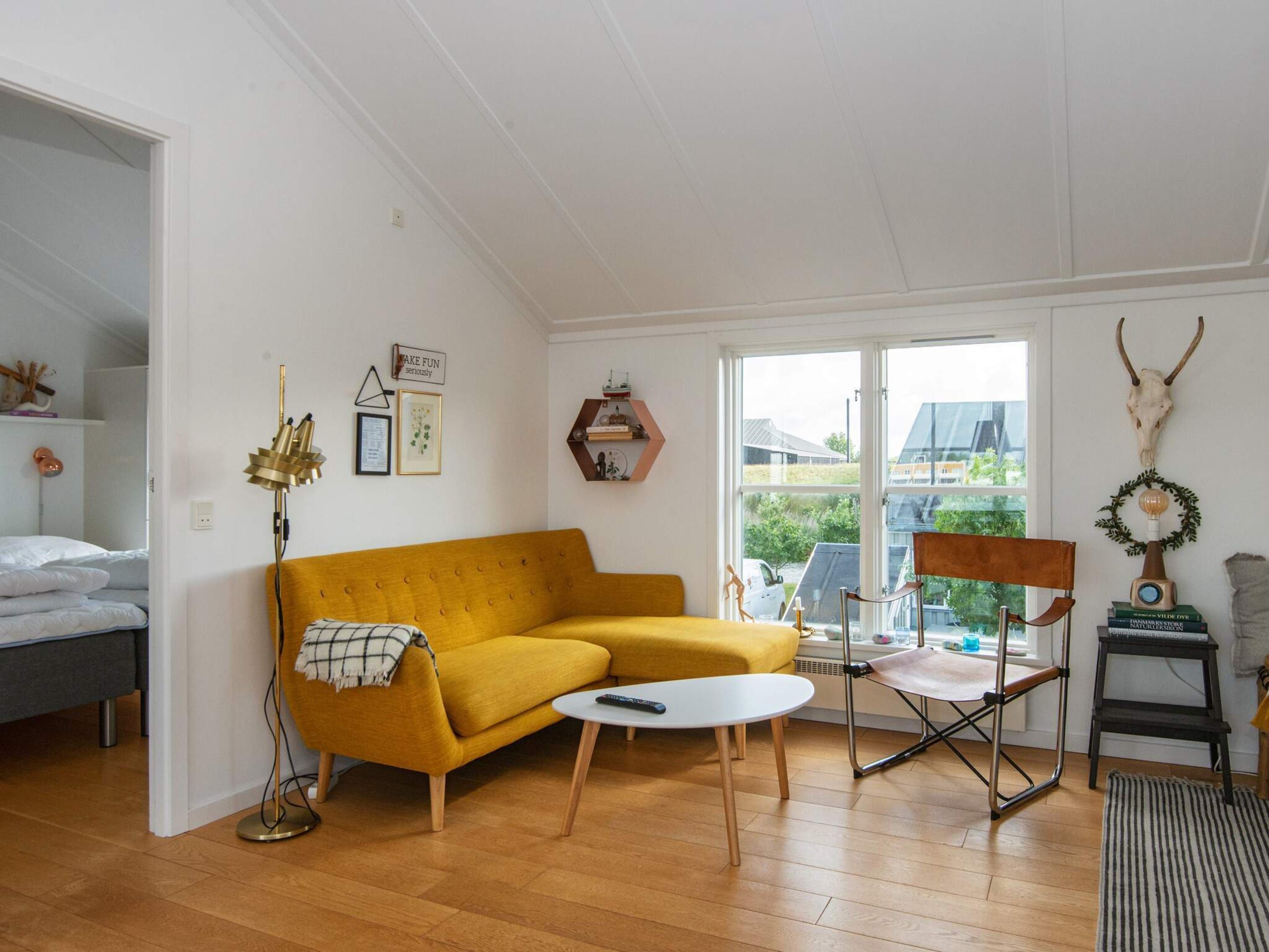 A living room with a sofa, a coffee table, and a chair. There is a window with a view of buildings outside.