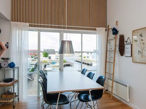 A dining area with a table and chairs, a view of the water and dock, and a wooden slatted ceiling. - Cosy Holiday Apartment in Ebeltoft (Ebeltoft)