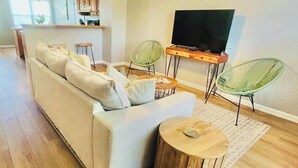 Un salon comprenant un canapé, deux fauteuils verts, une table basse en bois et un téléviseur posé sur un meuble.