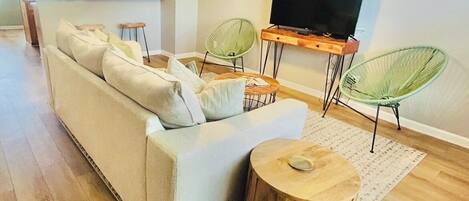 Een woonkamer met een bank, twee groene fauteuils, een houten salontafel en een televisie op een meubel.