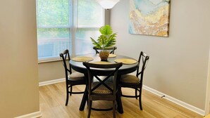 Un coin repas avec une table ronde, quatre chaises, une plante en pot et un tableau accroché au mur.