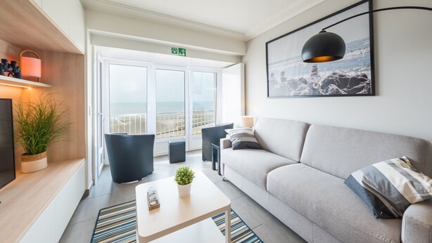 A modern living room with a sofa, a coffee table, and a TV. There is a balcony with a view of the sea. - Studio on the 3rd Floor With Phenomenal sea View (Middelkerke)