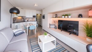 A modern living room with a sofa, coffee table, and TV. There is a kitchen area with a dining table and chairs. - Studio on the 3rd Floor With Phenomenal sea View (Middelkerke)