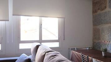 A room with a large window, a sofa, a dining table, and a potted plant.