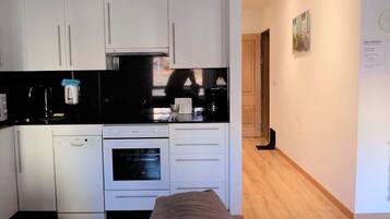 A compact kitchen with white cabinets, a black countertop, a dishwasher, and an oven.