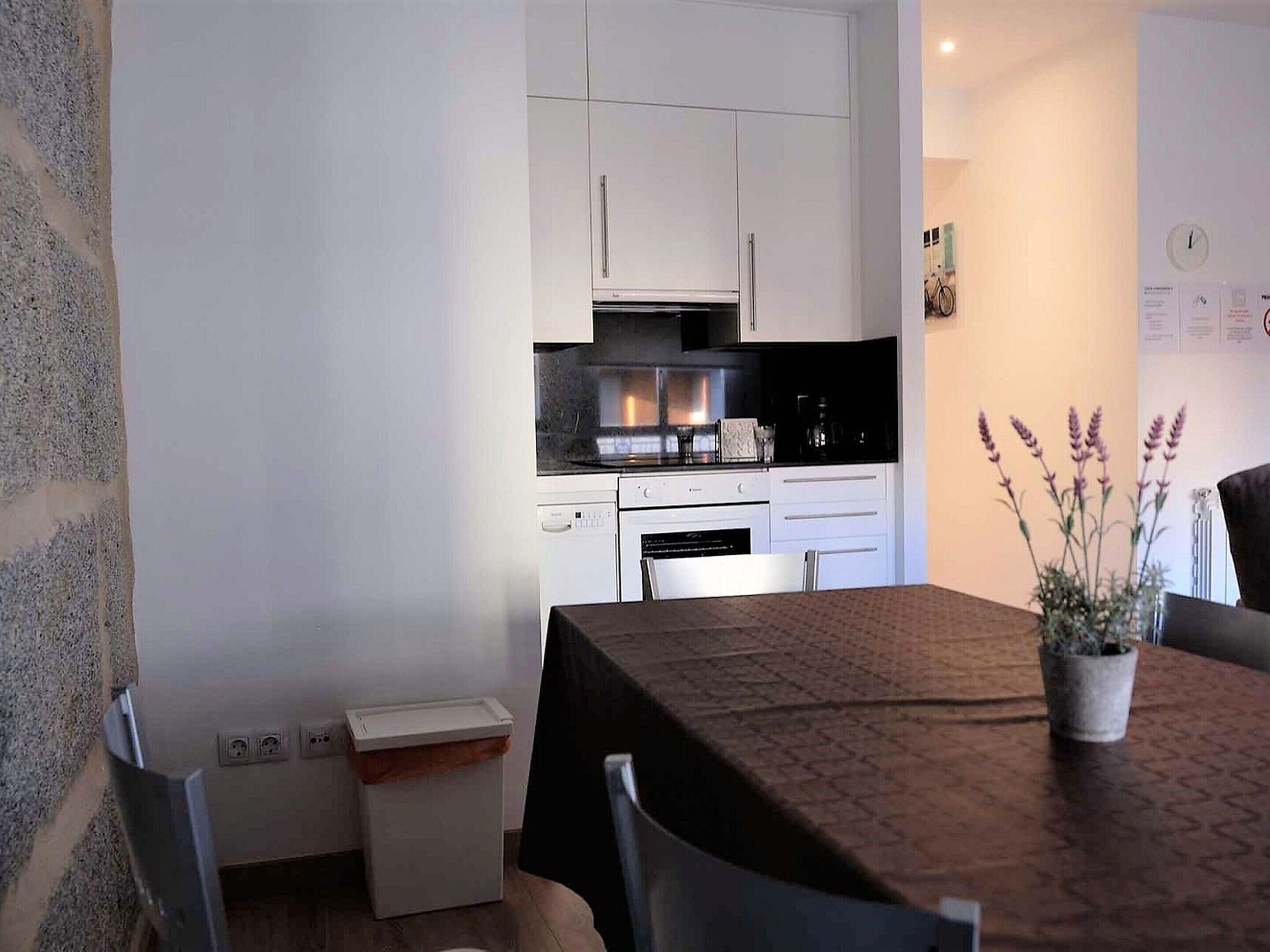 A compact kitchen with white cabinets, a stove, and a microwave. There is a small trash bin and a table with chairs.