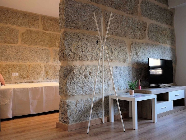 A modern living room with a stone wall, a TV, a white desk, and a sofa.