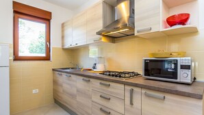 A modern kitchen with wooden cabinets, a gas stove, a microwave, and a window with blinds. - Apartment in Croatia Near the Coast (Medulin)