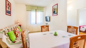 A dining area with a table set for four, a sofa with floral cushions, and a television on the wall. - Apartment in Croatia Near the Coast (Medulin)