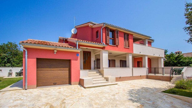 A two-story house with a red facade, a stone-paved driveway, and a visible garage door. - Apartment in Croatia Near the Coast (Medulin)
