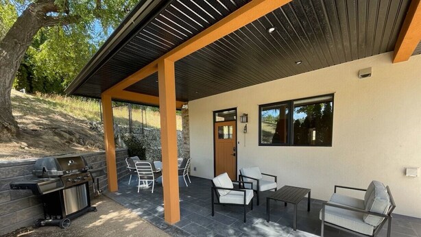 A covered patio with a grill, outdoor seating, and a door leading to the house.