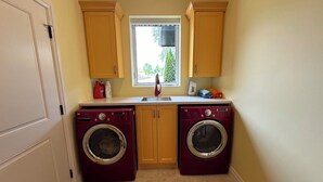 A laundry room with two front-loading washing machines, a window above the sink, and wooden cabinets.