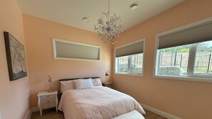 A bedroom with a bed, bedside tables, a hanging light fixture, and windows with blinds.