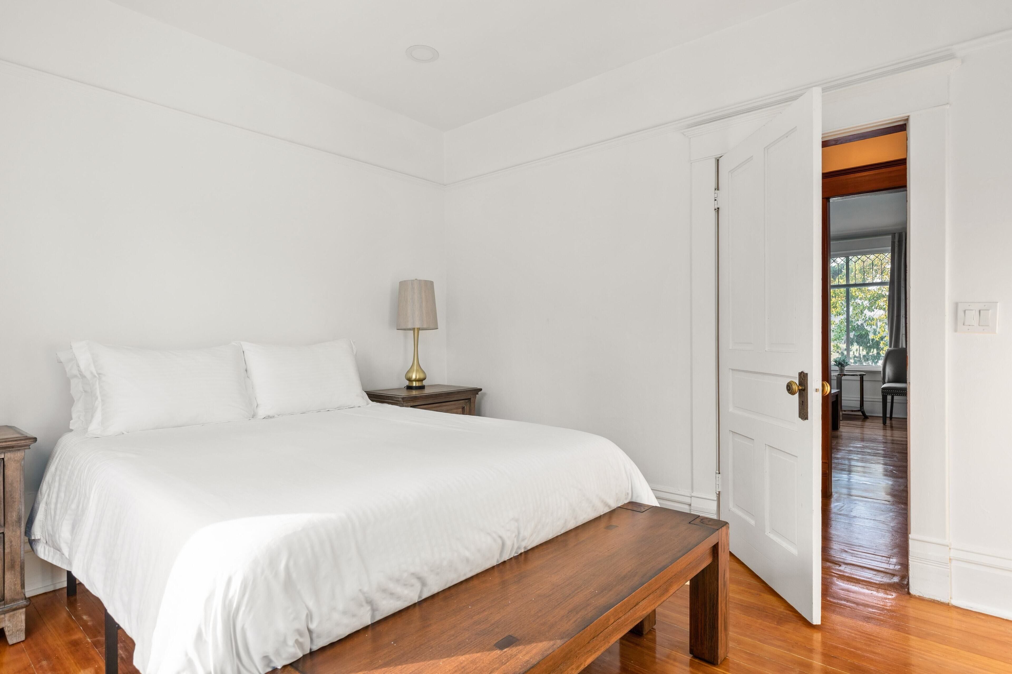 A bedroom with a large bed, a bedside table with a lamp, and a wooden bench.